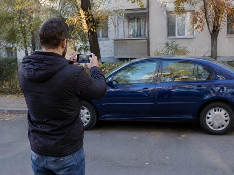 Un bărbat își fotografiază cu telefonul mașina parcată, ca s-o pună la vânzare