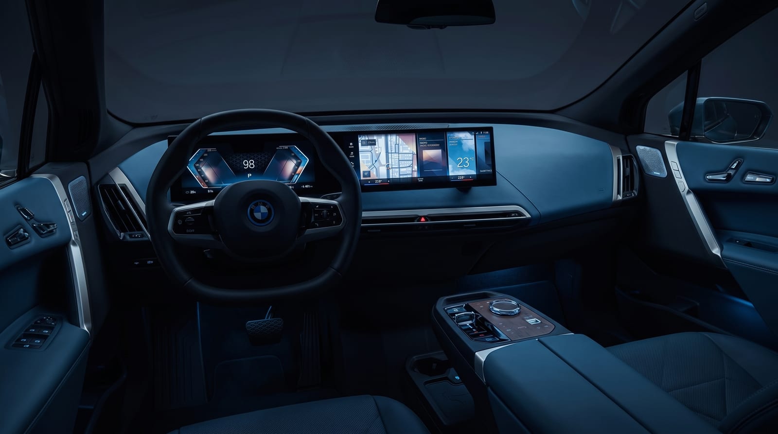 Bordul unui BMW cu ecranul curbat iDrive aprins, văzut de pe locul șoferului, noaptea, în lumină rece albastră